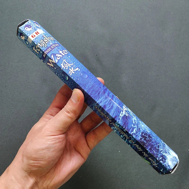 Blue incense box with text held by a hand against a dark background
