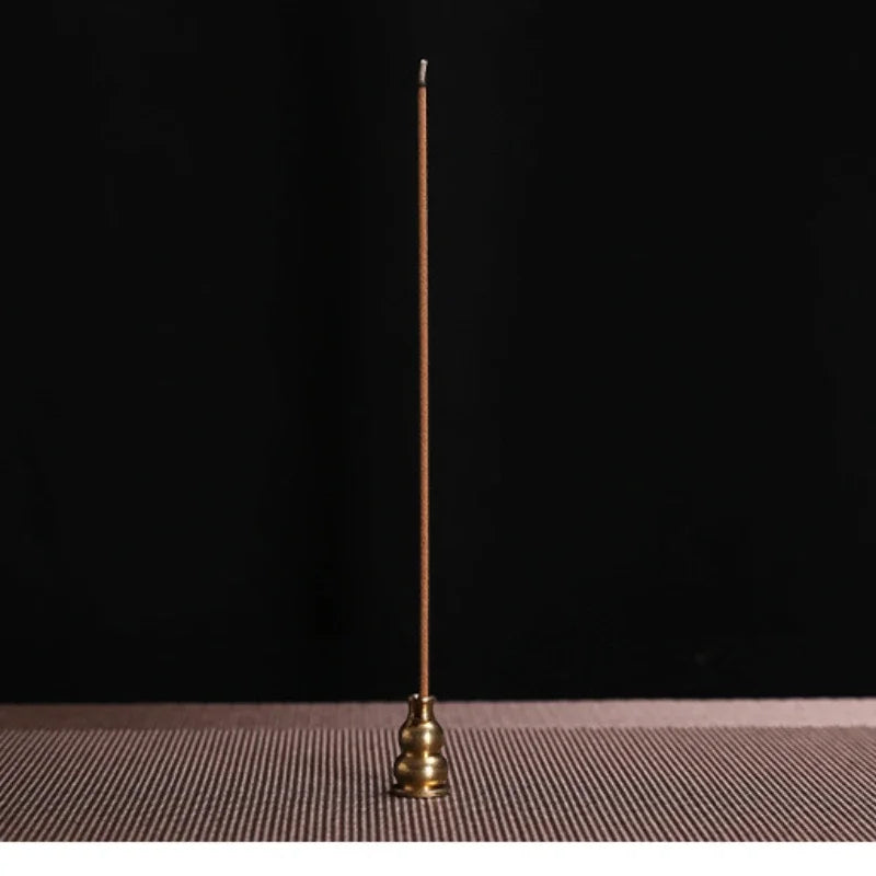 Brass incense stick holder with a single incense stick on a dark background
