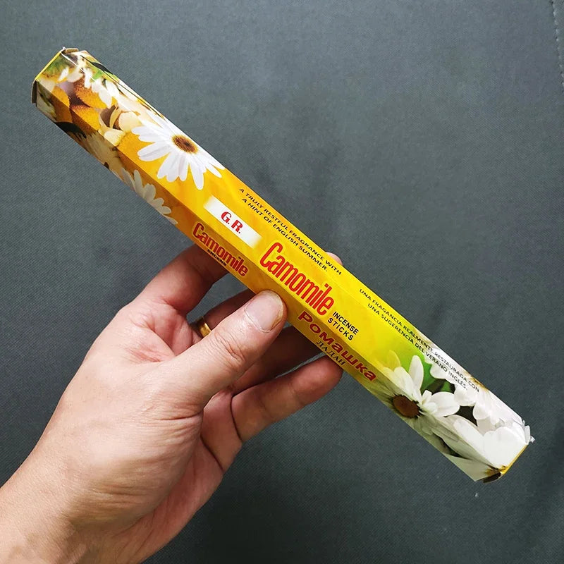 Hand holding a box of G.R. Camomile incense against a dark background