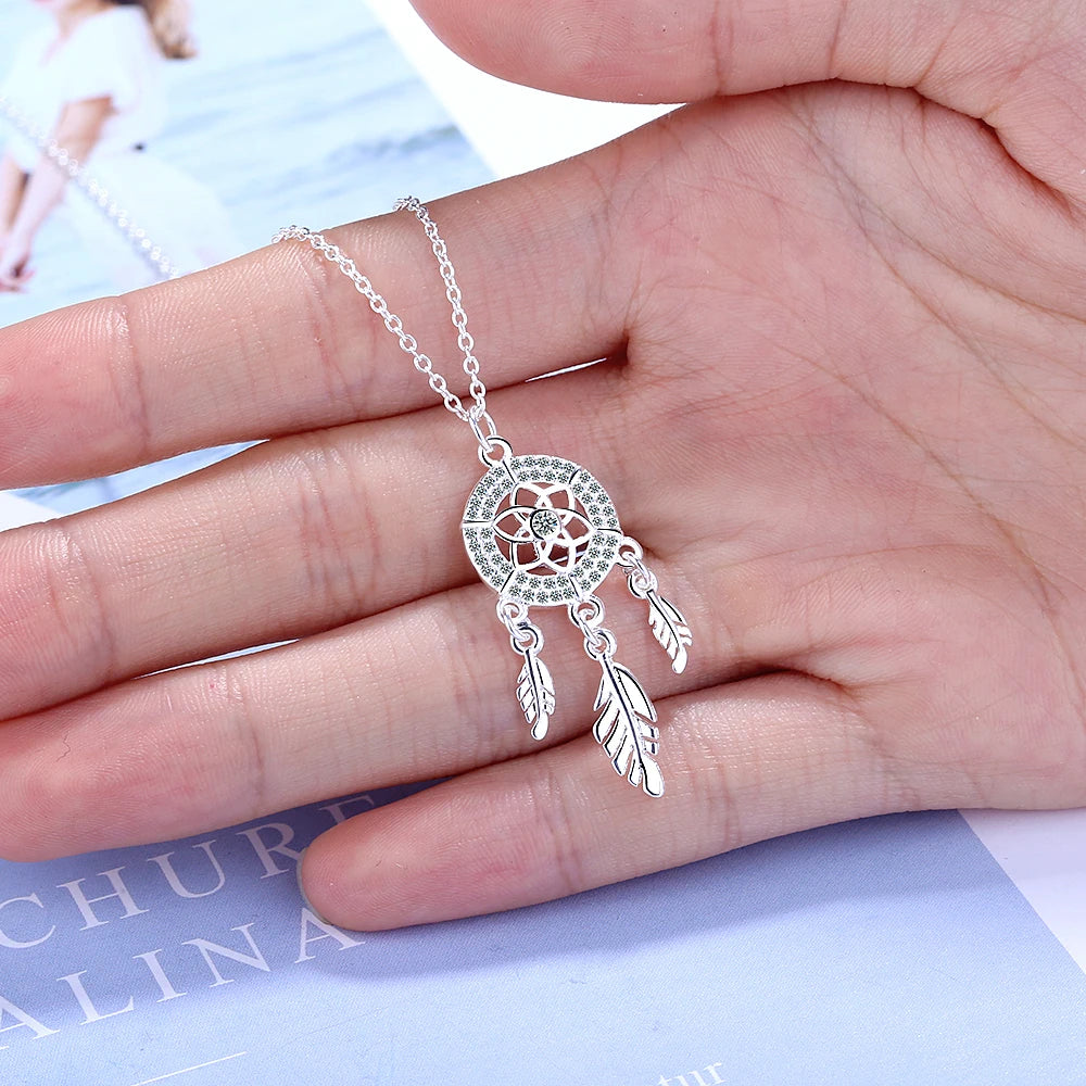 Silver necklace with a dreamcatcher pendant held in a hand against a light background