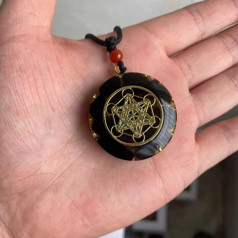 Black and gold pendant on a string held in a hand
