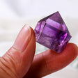 Amethyst crystal held between fingers against a white background