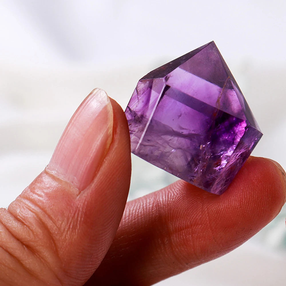 Amethyst crystal held between fingers against a white background