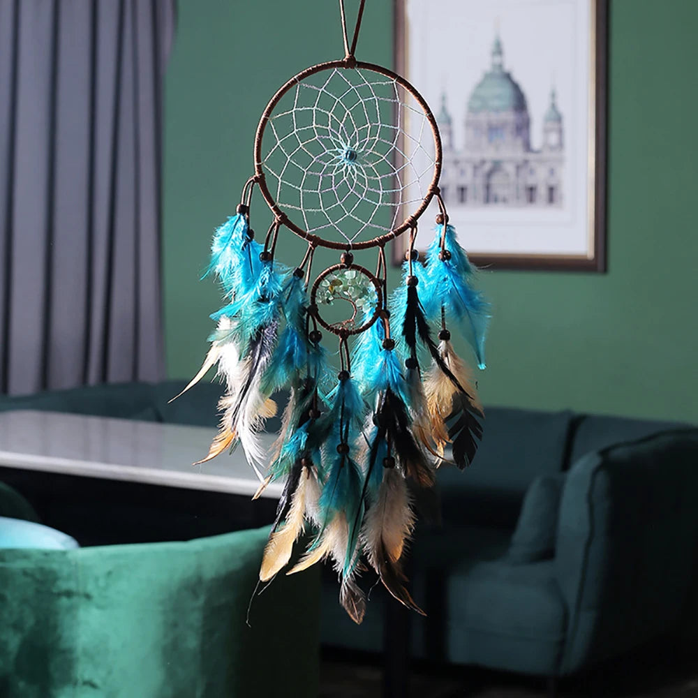 Dreamcatcher with blue feathers hanging in a room with a green wall and framed picture.