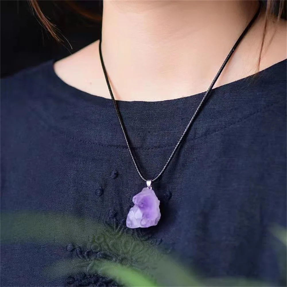 Person wearing a necklace with a purple pendant against a dark background
