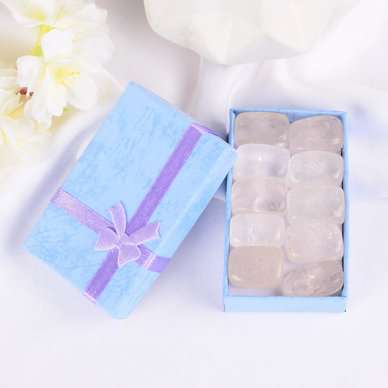 Set of white stones in a blue gift box with a purple ribbon on a white background with flowers.