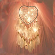 Heart-shaped dreamcatcher with lights against a soft pink background