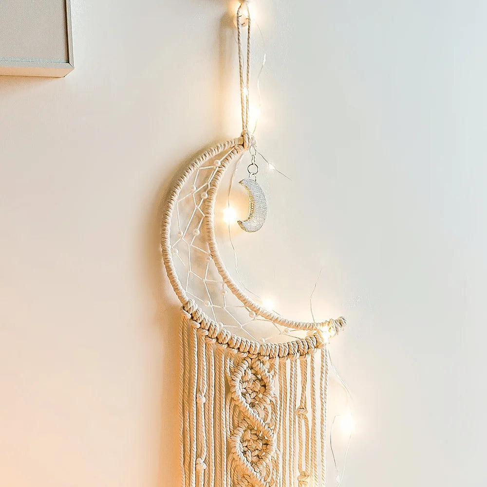 Decorative wall hanging with a moon-shaped design and string lights on a plain wall.