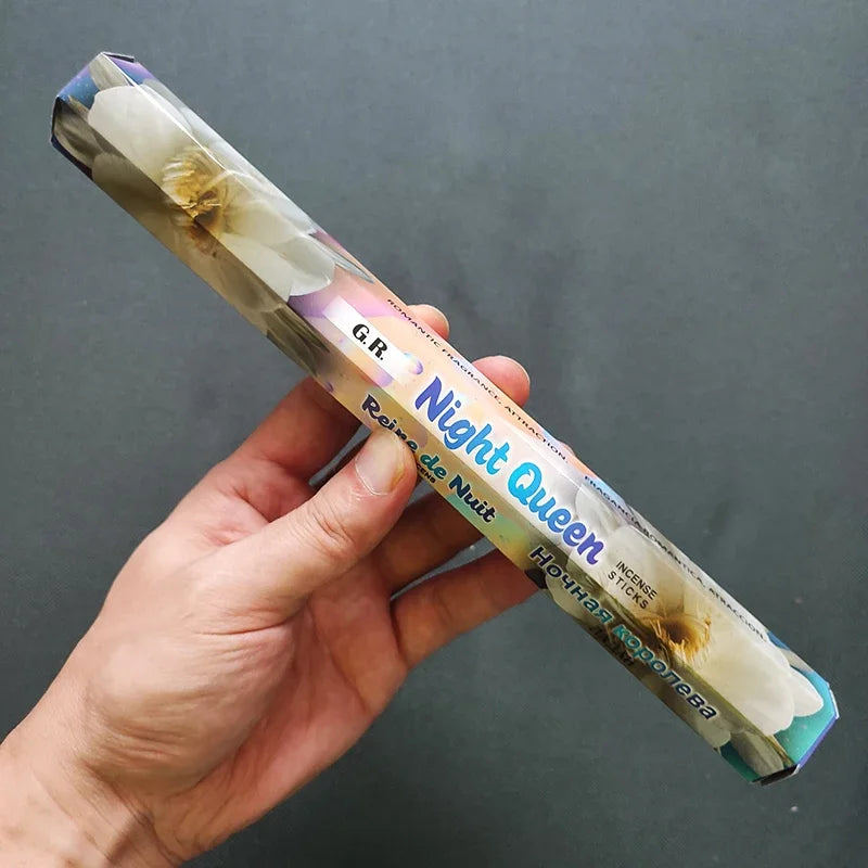 Hand holding a 'Night Queen' incense stick with a gray background