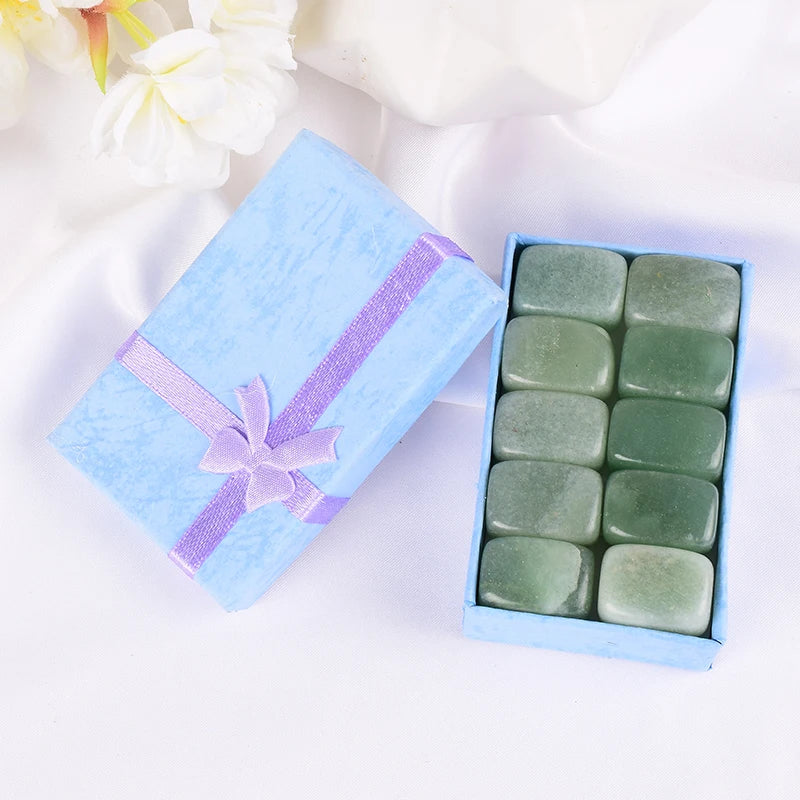 Open light blue gift box with a purple ribbon containing green stones on a white background.