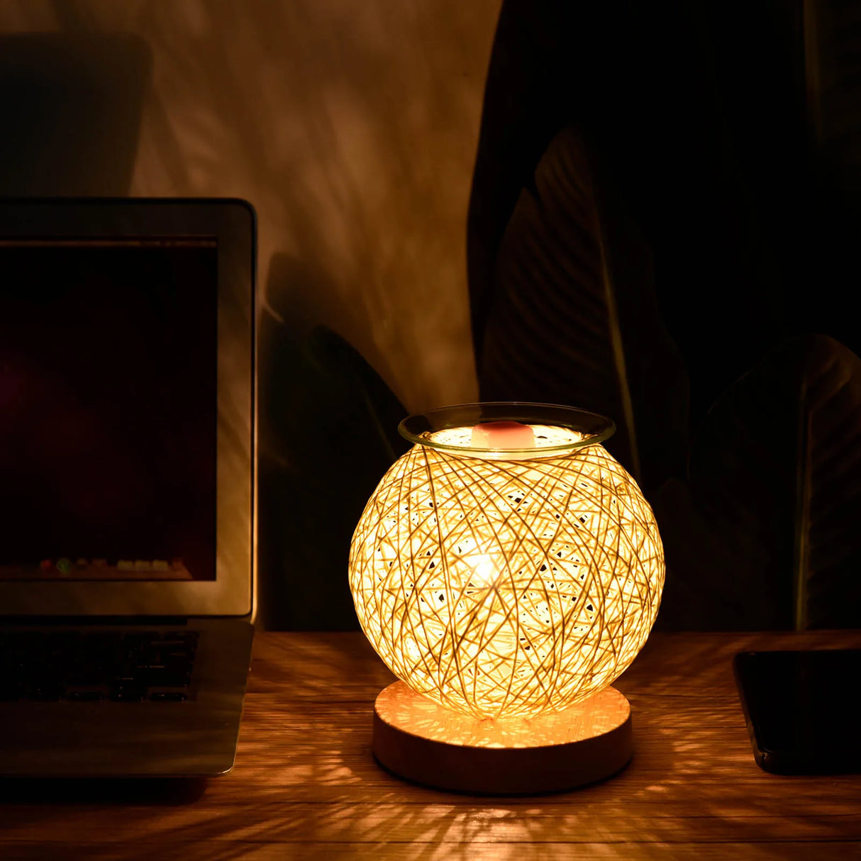 Round woven lamp on a desk next to a laptop in a dimly lit room