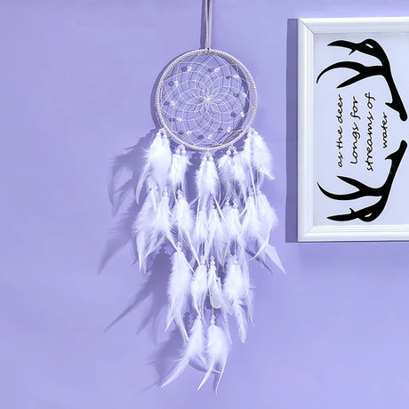 White dreamcatcher with feathers hanging on a purple wall next to a framed quote.
