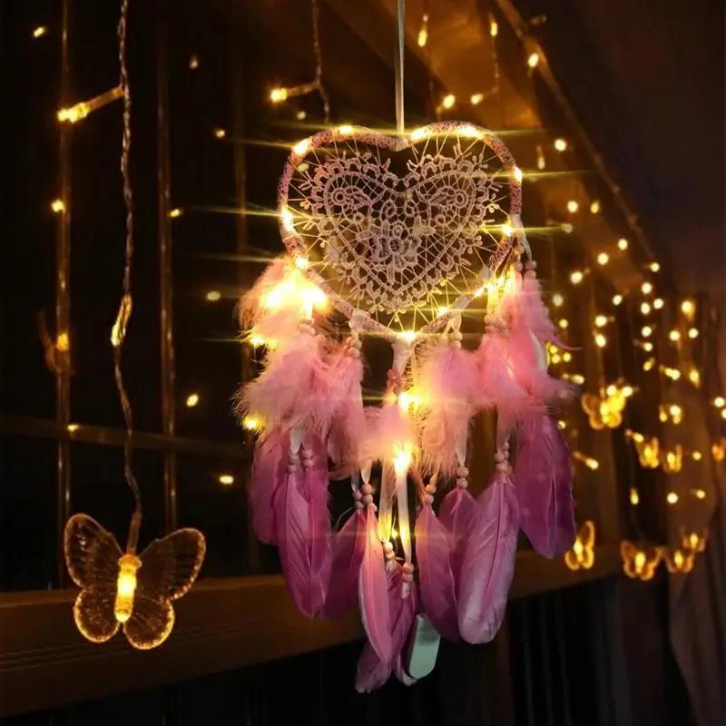 Decorative heart-shaped dreamcatcher with feathers and fairy lights against a dark background