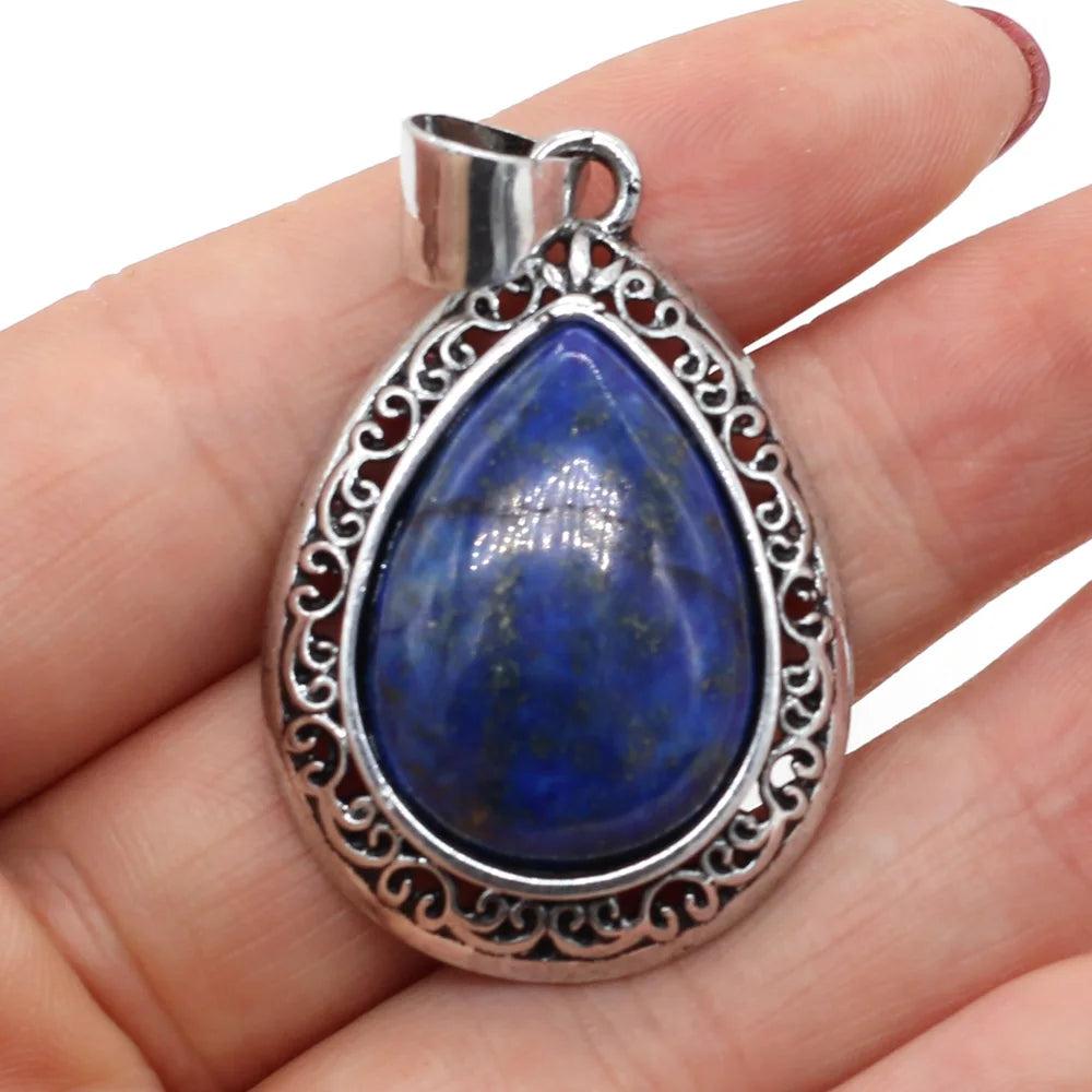 Teardrop-shaped blue stone pendant with silver frame held in hand against a white background