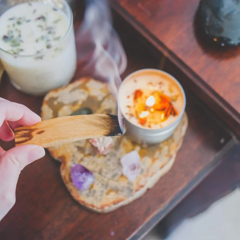 Person lighting a candle on a wooden coaster with a glass of milk and cookies in the background.