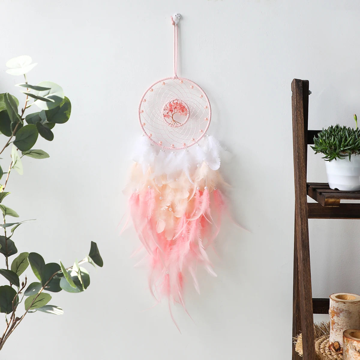 Decorative dreamcatcher with pink and white feathers hanging on a white wall.