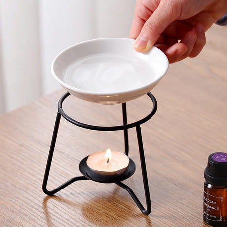 Person using a white ceramic dish on a black essential oil burner with a lit candle below.