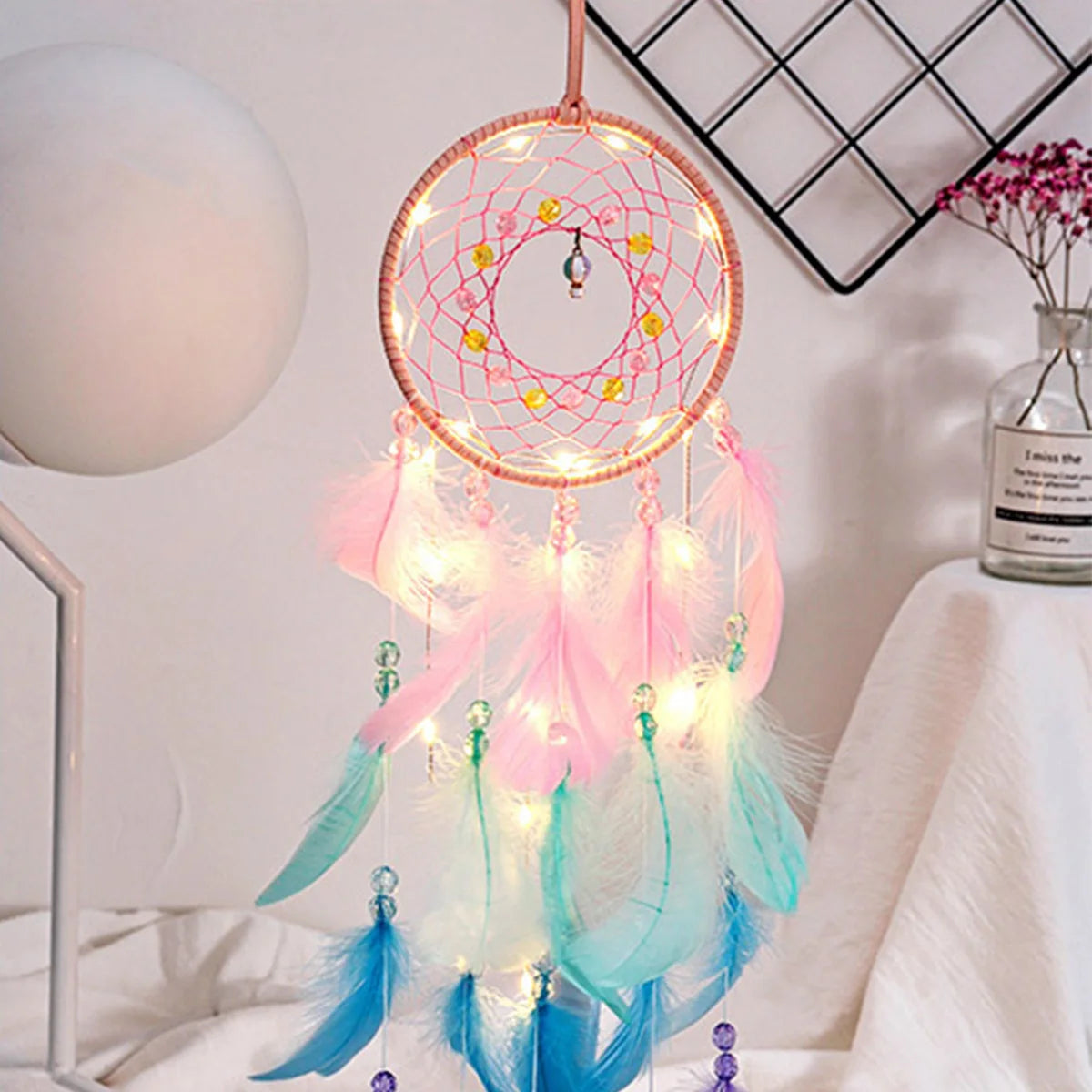Decorative dreamcatcher with lights and feathers on a white surface.