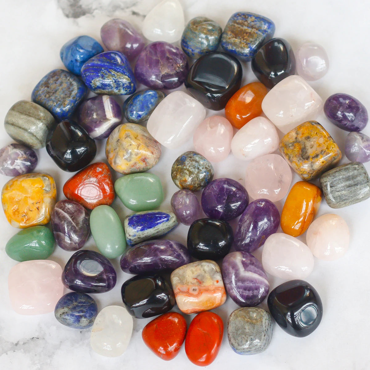 Assorted colorful tumbled stones on a white marble surface