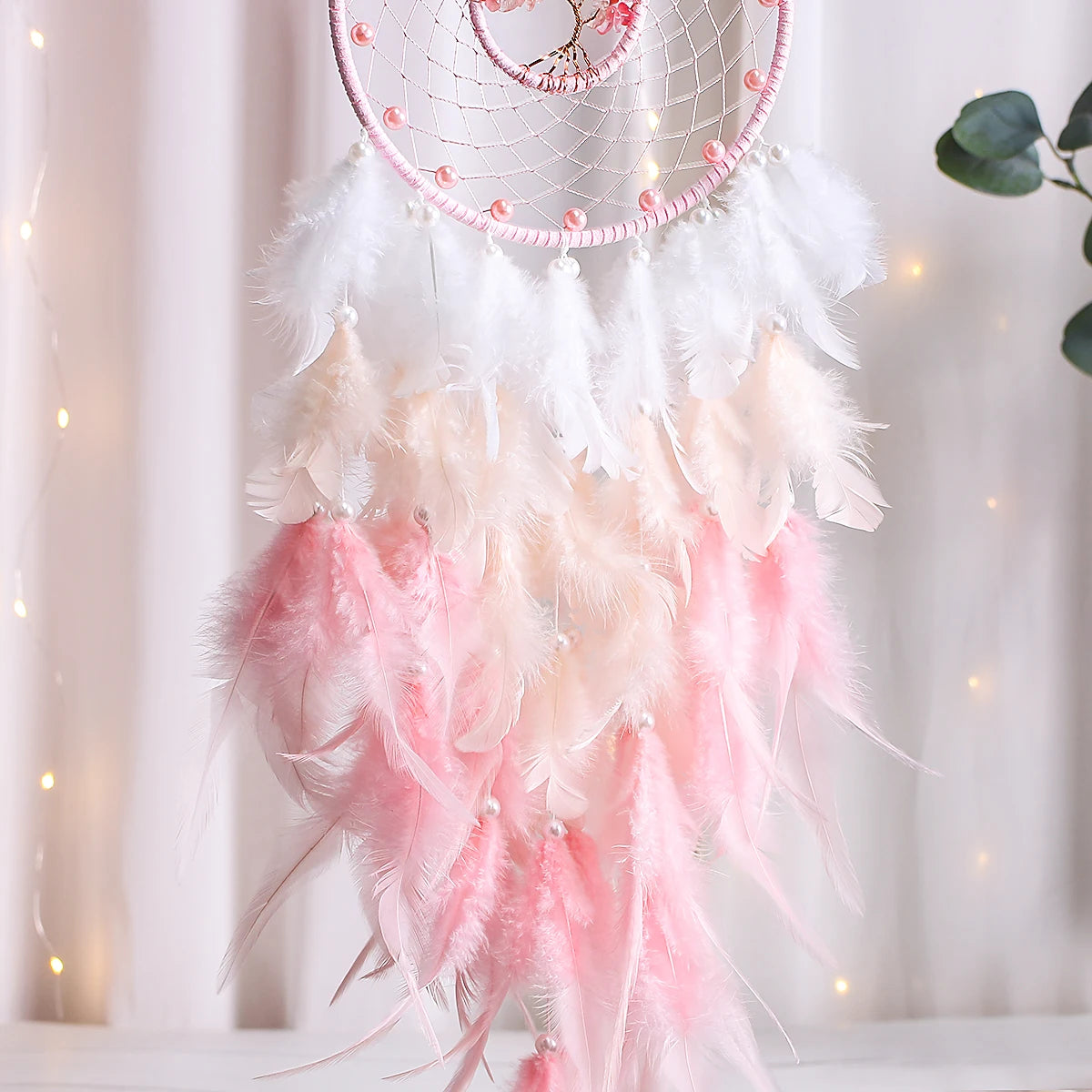 Pink and white dreamcatcher with feathers against a light background