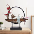 Decorative piece with a figure, cherry blossoms, and a circular design on a wooden surface.