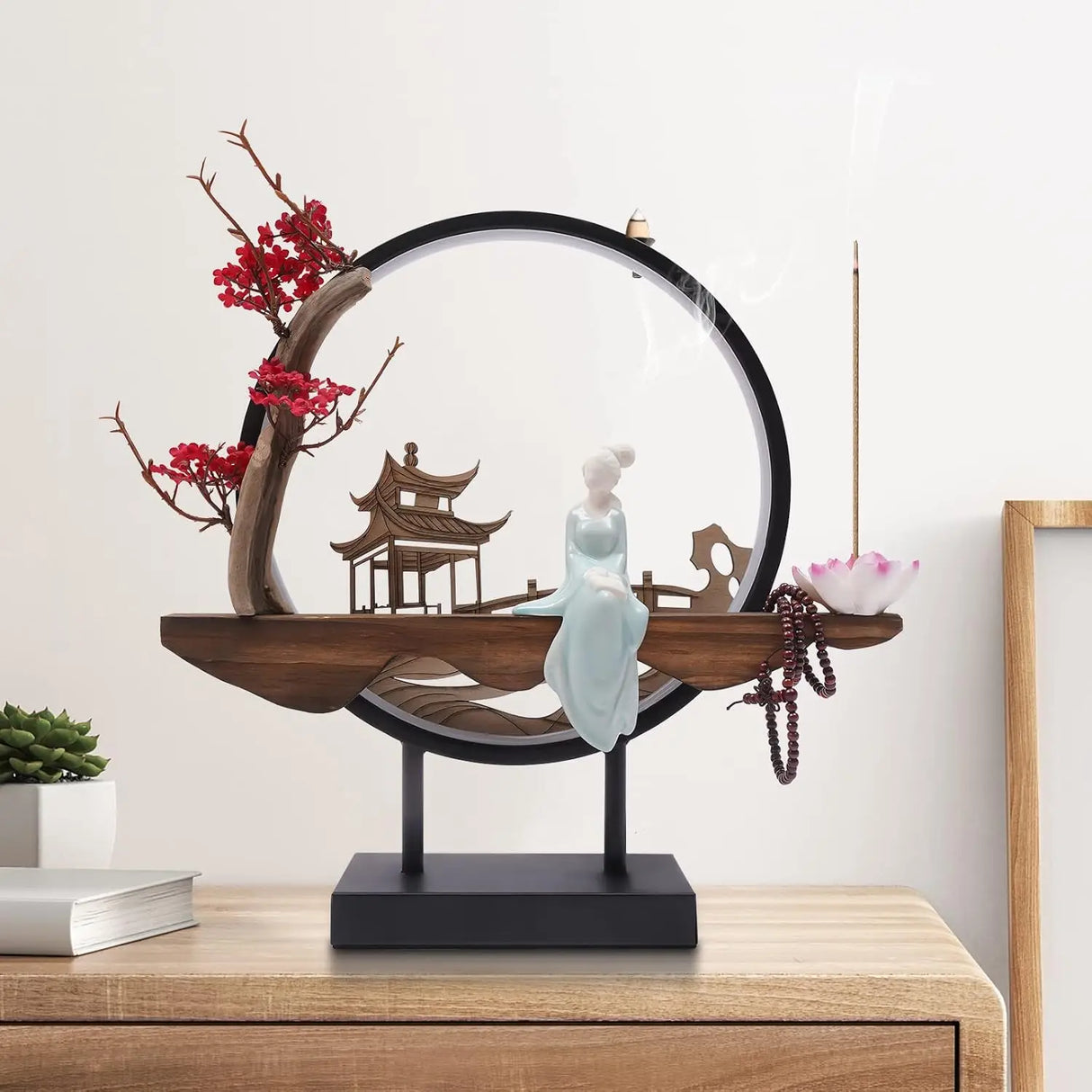 Decorative piece with a figure, cherry blossoms, and a circular design on a wooden surface.