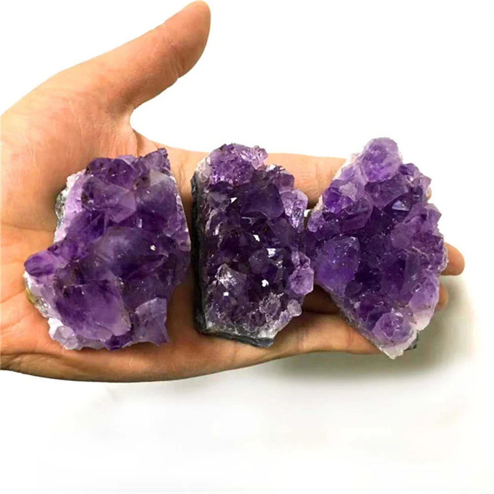 Three purple amethyst crystals held in a hand against a white background