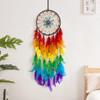 Colorful dreamcatcher hanging on a wall with a bed and plant in the background