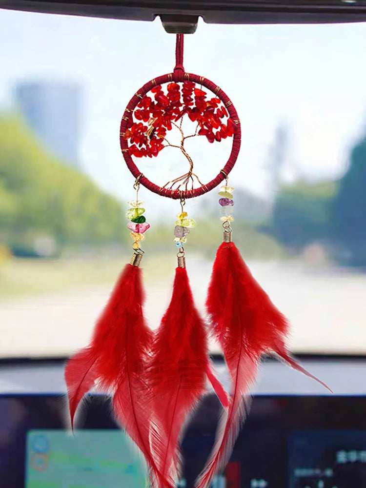 Red feathered car ornament hanging from a car's rearview mirror with a blurred outdoor background.