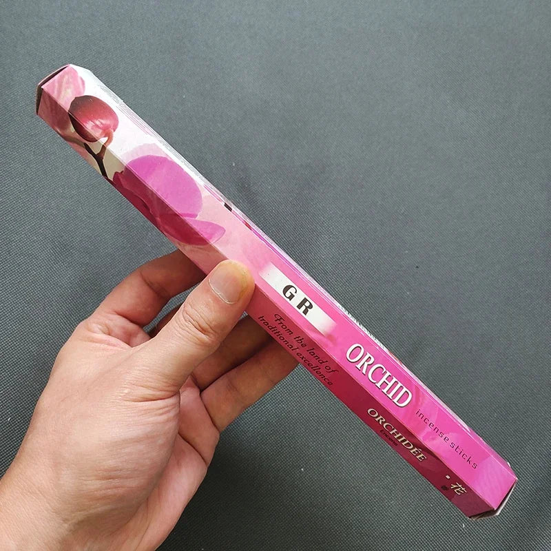 Hand holding a pink orchid incense stick box against a gray background