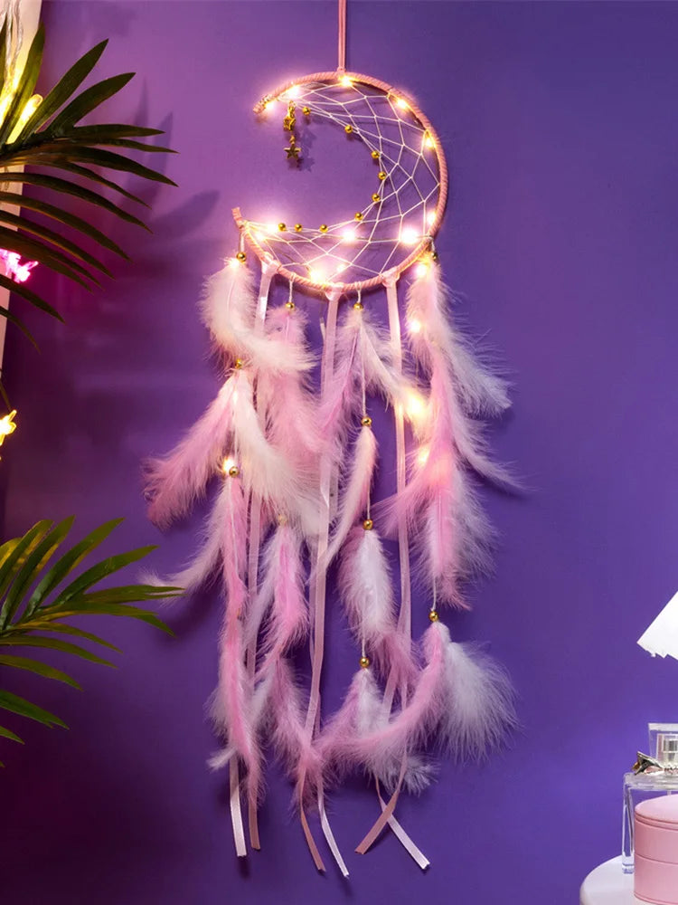 Decorative dreamcatcher with pink feathers and fairy lights against a purple wall.