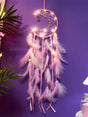 Decorative dreamcatcher with pink feathers and fairy lights against a purple wall.