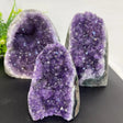 Three purple amethyst geodes on a dark surface with a white background