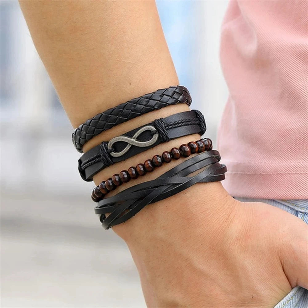Multiple black leather bracelets with a silver infinity symbol on a wrist against a blurred background.