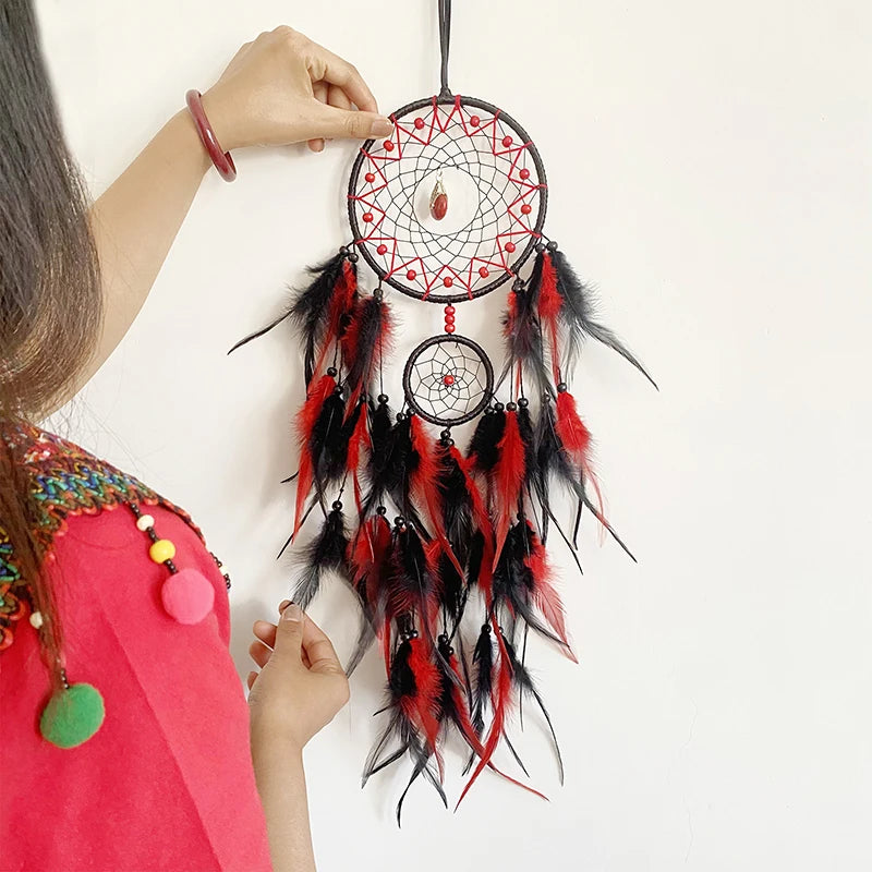 Handmade dreamcatcher with red, black, and white feathers held by a person against a white background