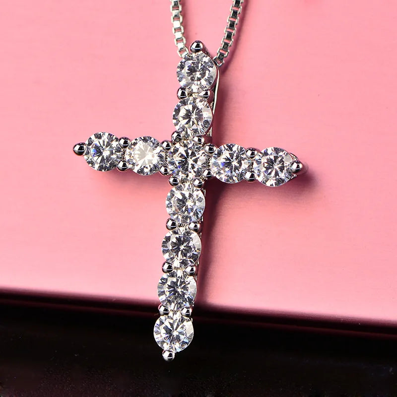 Silver cross pendant with clear stones on a pink background
