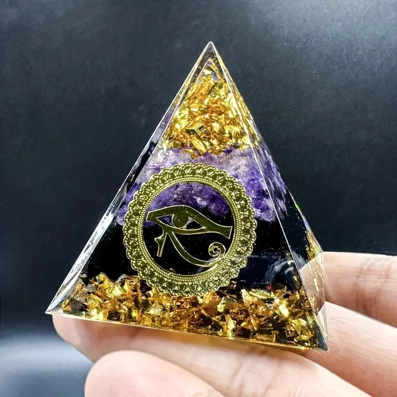 Pyramid-shaped crystal with Eye of Horus design held by a hand against a dark background