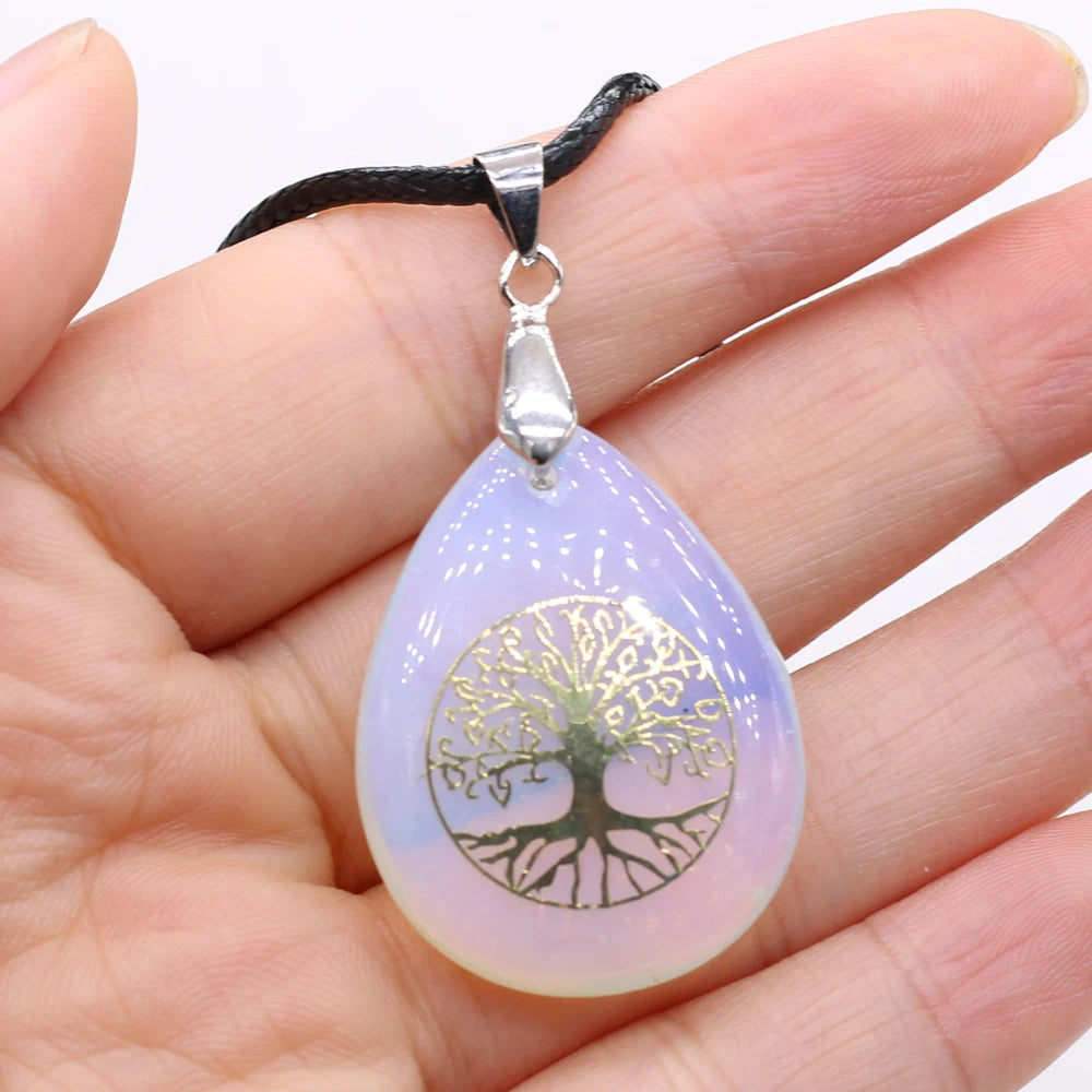 Teardrop-shaped pendant with tree of life design held in a hand against a white background