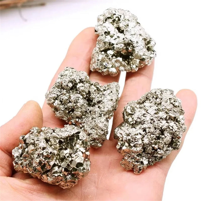 Hand holding four metallic pyrite crystals against a white background