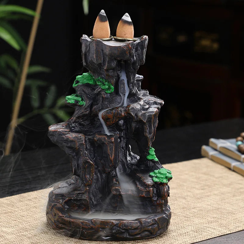 Decorative incense burner shaped like a mountain with two incense sticks on top.