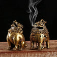 Two ornate brass incense burners on a wooden surface with a dark background