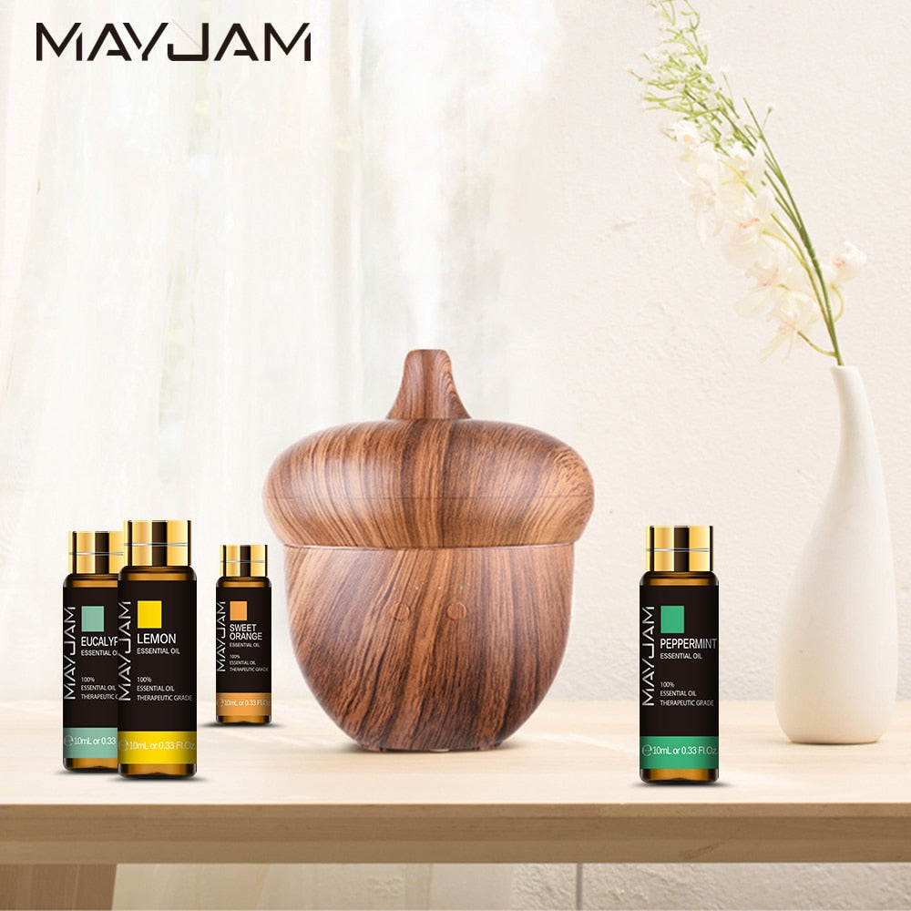 Wooden diffuser and Mayjam essential oil bottles on a table with a vase in the background.