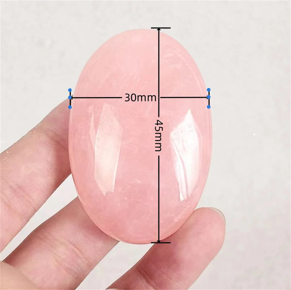 Pink oval stone held between fingers with measurements indicated