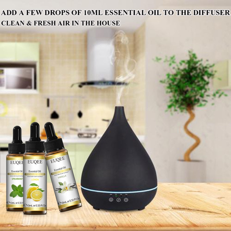 Black essential oil diffuser on a wooden surface with three bottles of essential oils in the background.