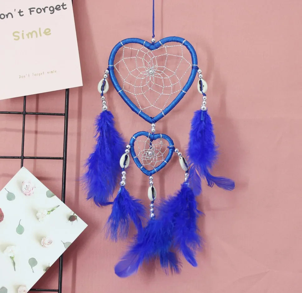 Blue heart-shaped dreamcatcher with feathers on a pink background