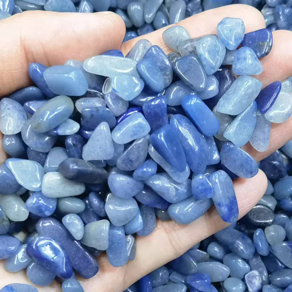Hand holding a small pile of blue pebbles with a background of more pebbles.