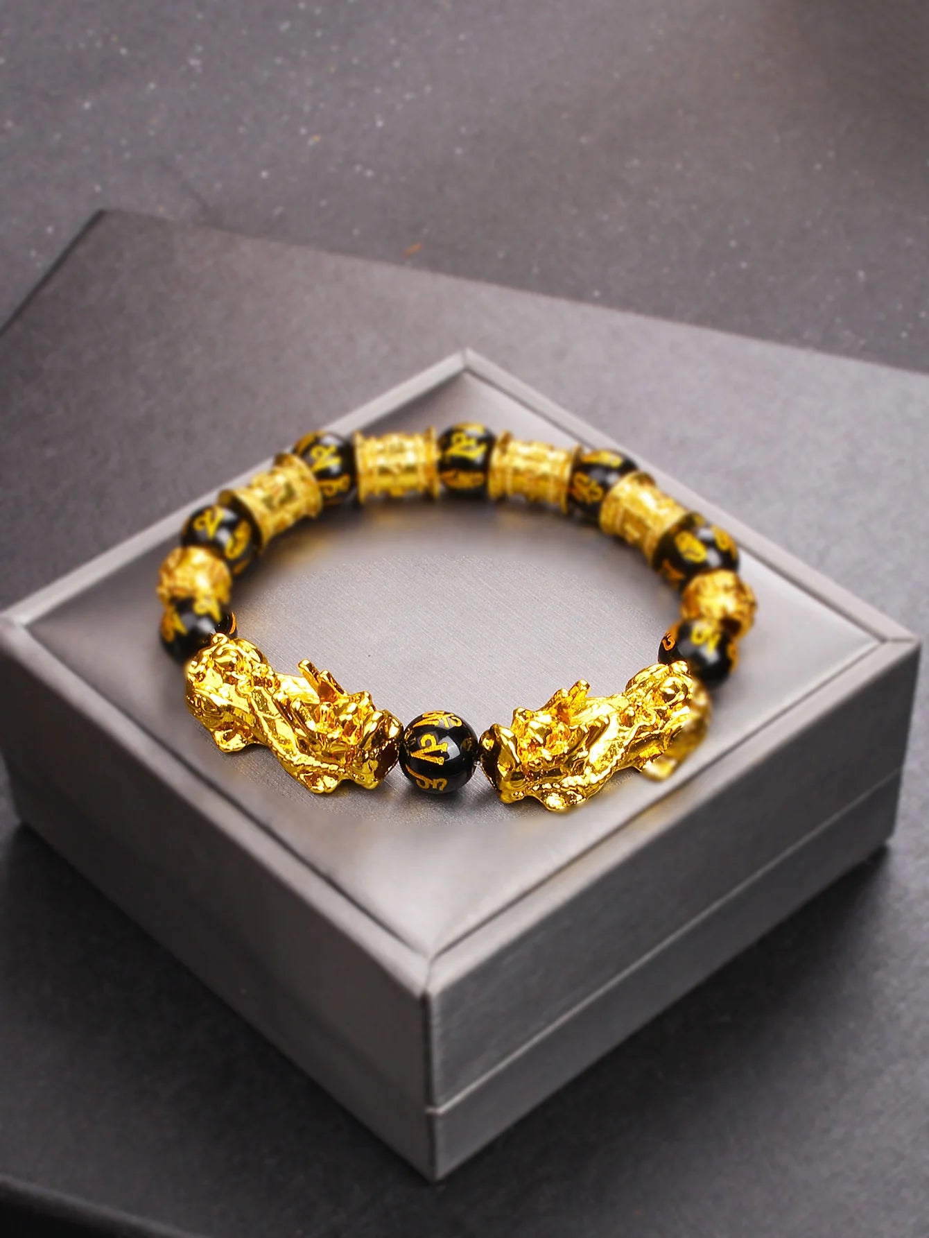 Gold and black beaded bracelet on a gray box
