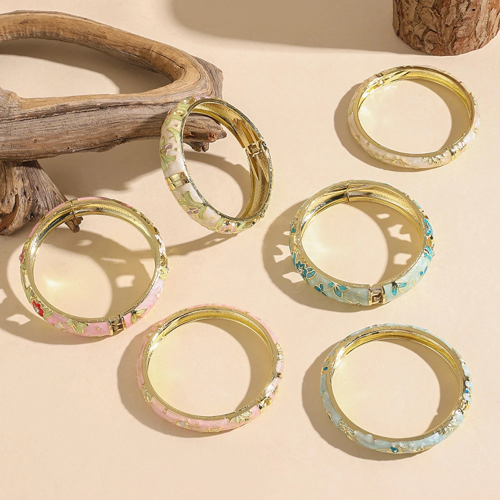 Set of gold bangles with floral patterns on a beige surface