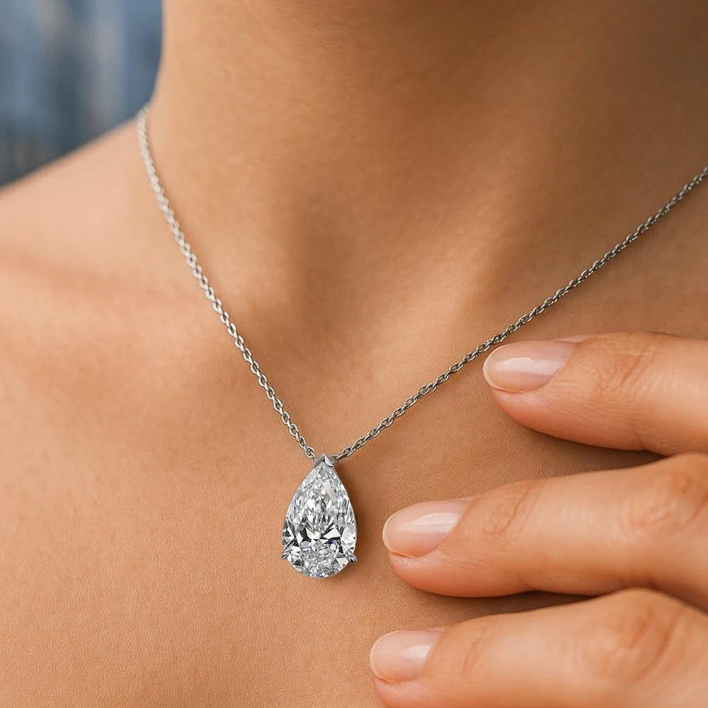 Teardrop-shaped diamond pendant on a chain, worn by a person.