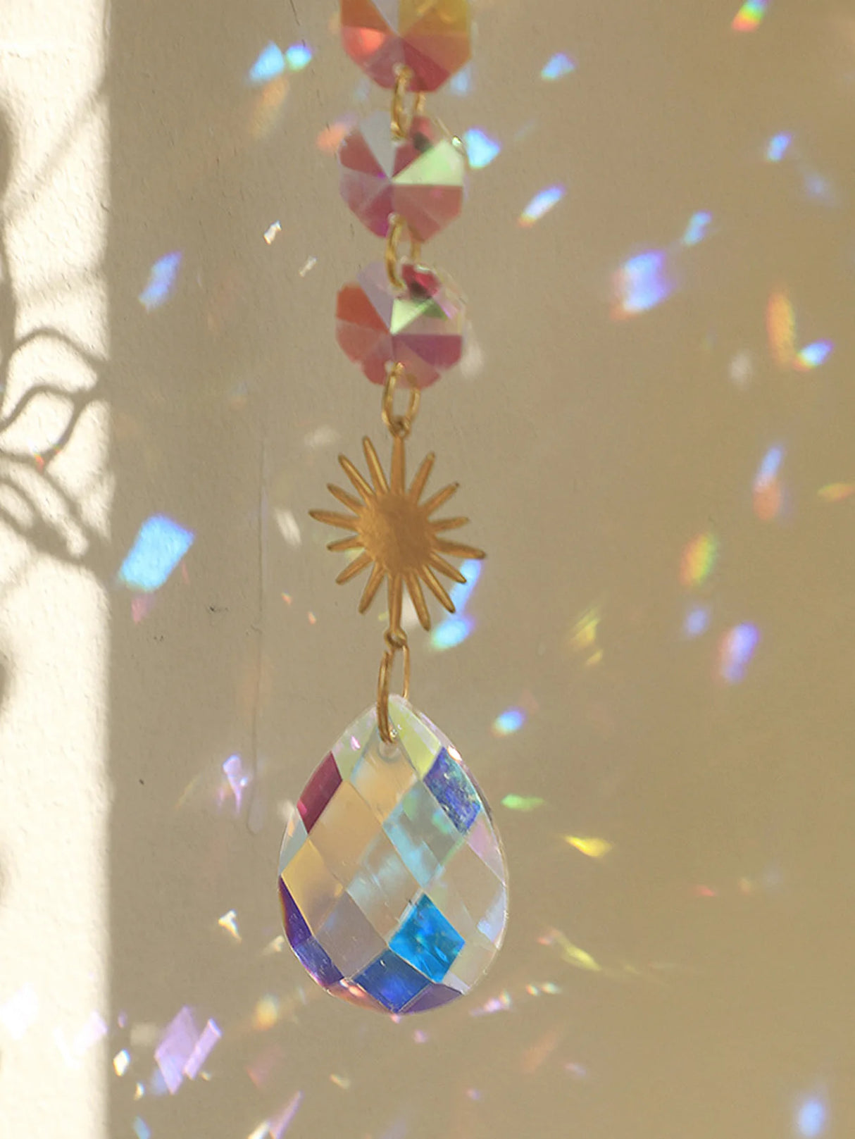 Colorful hanging crystal with a gold sun-shaped charm against a neutral background